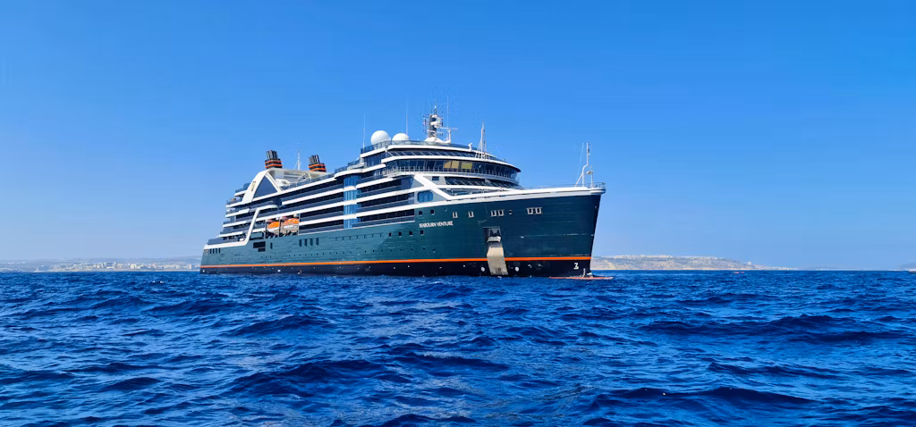Seabourn Venture in blue seas with coastline in the background